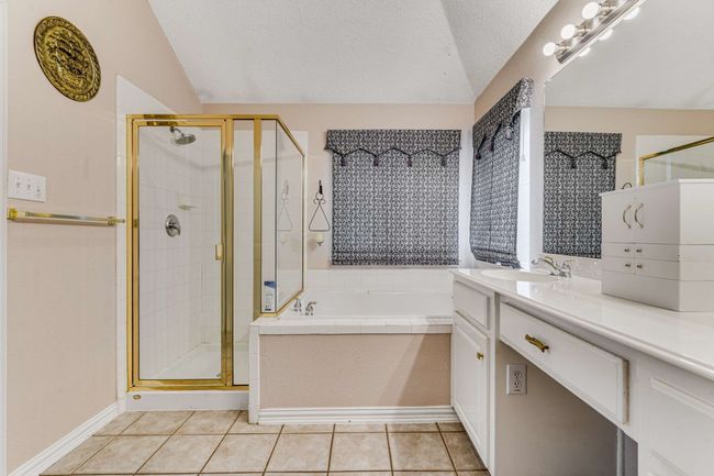 Full bathroom featuring a garden tub, a separate shower, separate sinks, tile patterned flooring, and vaulted ceiling. | Image 25