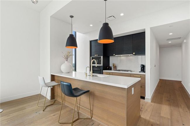 Kitchen with a sink, light countertops, light wood-style flooring, stainless steel gas stovetop, and dark cabinets | Image 8