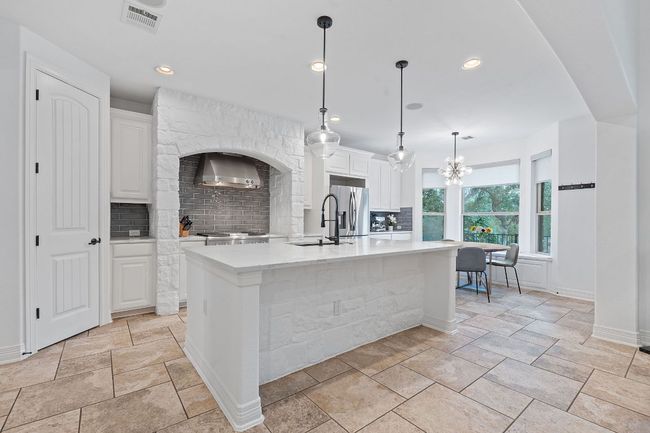 Kitchen featuring stainless steel refrigerator with ice dispenser, a sink, decorative backsplash, wall chimney exhaust hood, and white cabinets | Image 12
