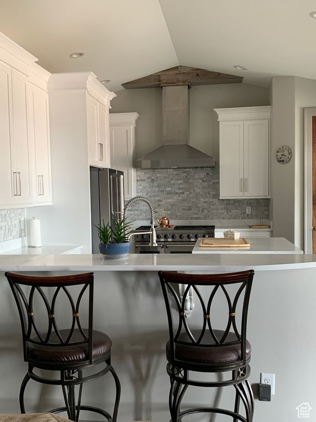 Kitchen with premium appliances, light countertops, white cabinetry, vaulted ceiling, and wall chimney exhaust hood | Image 4