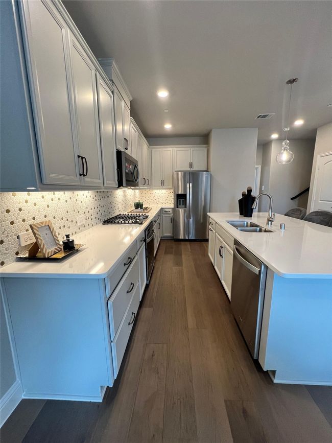 Kitchen featuring dark wood-style floors, tasteful backsplash, stainless steel appliances, light countertops, and a kitchen island with sink | Image 5