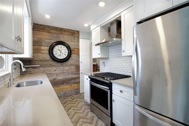 Kitchen with appliances with stainless steel finishes, a sink, wood walls, wall chimney range hood, and tasteful backsplash | Image 11