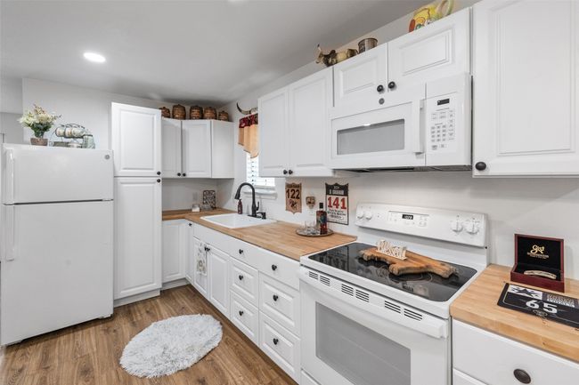 Kitchen with white appliances, butcher block counters, white cabinetry, wood finished floors, and a sink | Image 30
