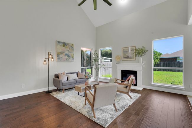 Living area with high vaulted ceiling, a glass covered fireplace, dark wood finished floors, and a ceiling fan | Image 13