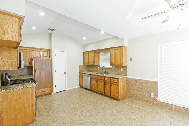Kitchen with stainless steel dishwasher, ceiling fan, light stone counters, backsplash, and vaulted ceiling | Image 10
