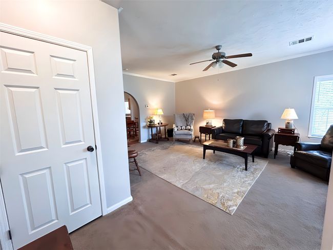 Living room featuring concrete flooring, crown molding, arched walkways, visible vents, and a ceiling fan | Image 12