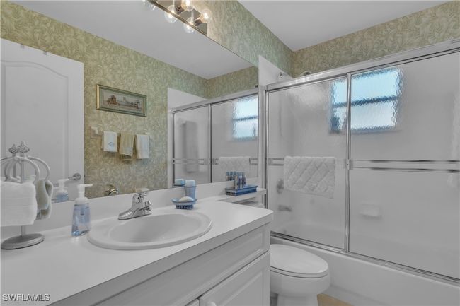 Full bath featuring wallpapered walls, vanity, shower / bath combination with glass door, and toilet | Image 23