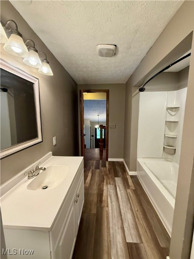 Bathroom with vanity, shower / bath combination, baseboards, a textured ceiling, and wood finished floors | Image 25