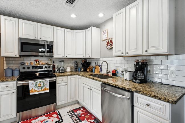 Kitchen featuring stainless steel appliances, white cabinets, light tile patterned flooring, decorative backsplash, and a textured ceiling | Image 8