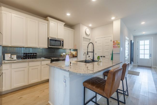 Kitchen featuring stainless steel microwave, light wood-style flooring, an island with sink, backsplash, and white cabinets | Image 9