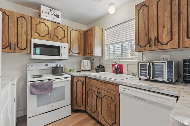 Kitchen with brown cabinets, a sink, white appliances, and independent washer and dryer | Image 18