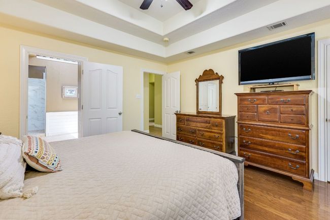 Bedroom featuring wood finished floors, a ceiling fan, and a tray ceiling | Image 10