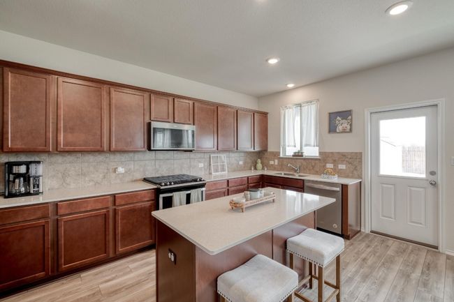 Kitchen with light countertops, a sink, tasteful backsplash, a breakfast bar, and appliances with stainless steel finishes | Image 15