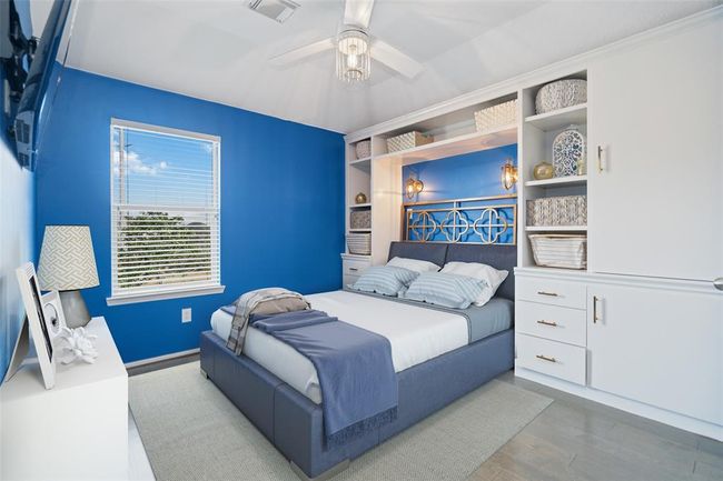 Bright, modern bedroom with vibrant blue walls and white built-in shelving. Features a cozy bed with stylish decor, ample storage, and natural light through a large window. | Image 37