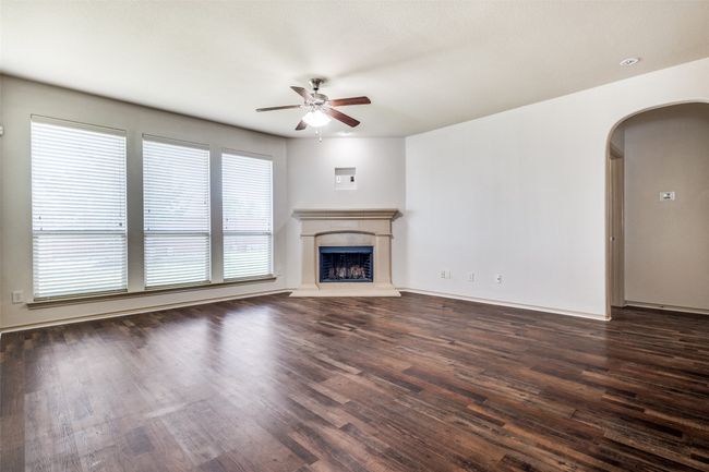 Unfurnished living room featuring ceiling fan, arched walkways, dark wood-type flooring, and a fireplace with raised hearth | Image 6