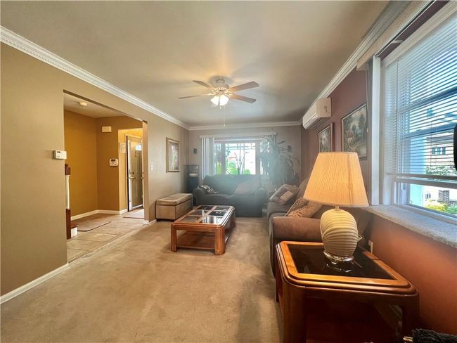Carpeted living room featuring ceiling fan, a wall unit AC, and ornamental molding | Image 4