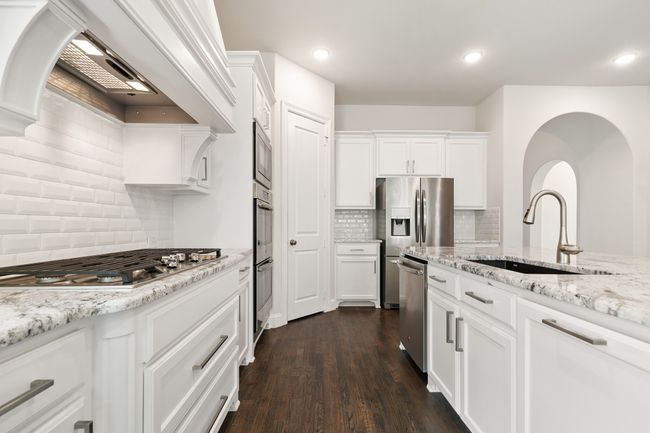 Kitchen with light stone counters, a sink, white cabinetry, appliances with stainless steel finishes, and dark wood-style flooring | Image 12