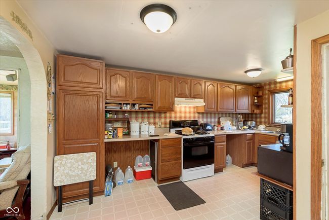 kitchen featuring open shelves, under cabinet range hood, gas stove, light countertops, and brown cabinets | Image 11