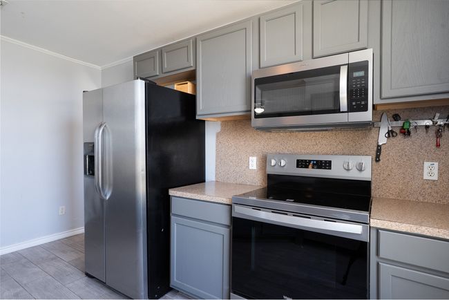 Kitchen with stainless steel appliances, gray cabinets, backsplash, ornamental molding, and light countertops | Image 13