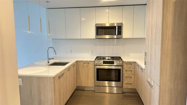 Kitchen featuring appliances with stainless steel finishes, modern cabinets, light countertops, light brown cabinets, and dark wood-type flooring | Image 8