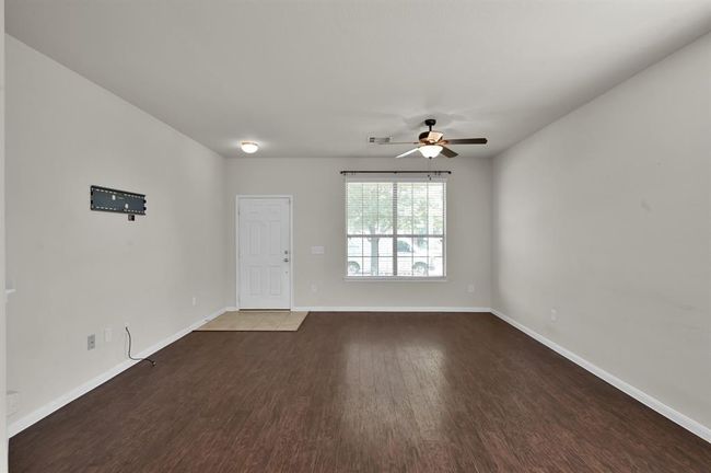Hardwood flooring, neutral walls, a large window for natural light, and a ceiling fan. T | Image 7
