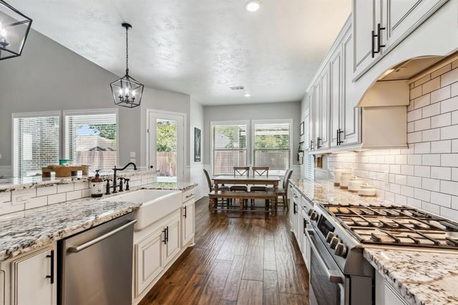 This kitchen combines functionality and style with its gas range featuring a vent hood cabinet and a beautiful farmhouse sink thoughtfully placed in the island. | Image 16