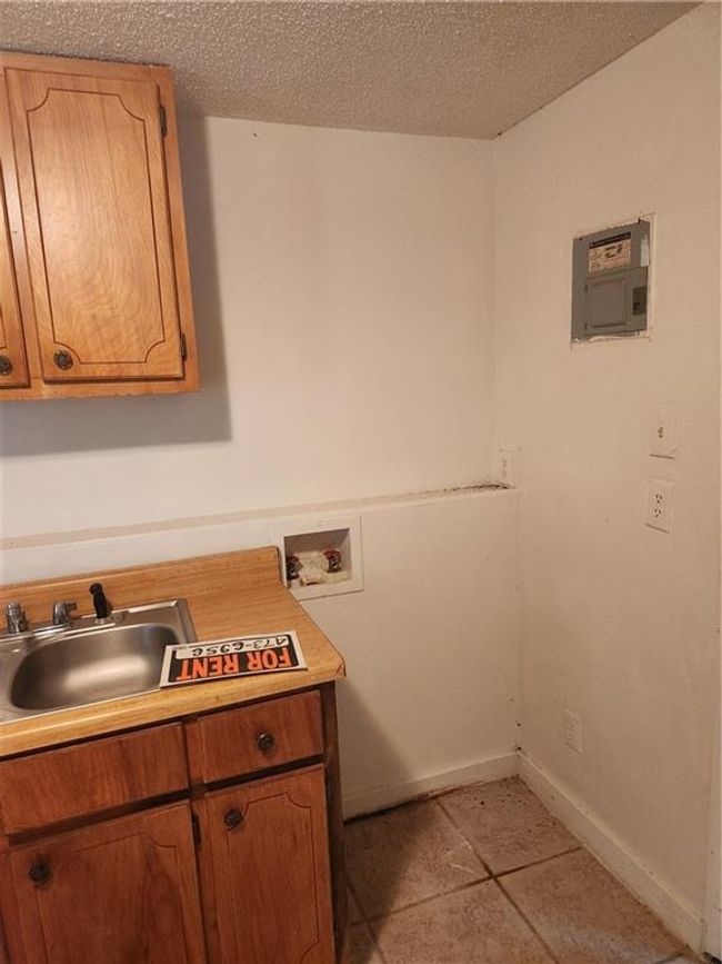 Laundry area with light tile patterned flooring, a textured ceiling, cabinets, washer hookup, and sink | Image 14