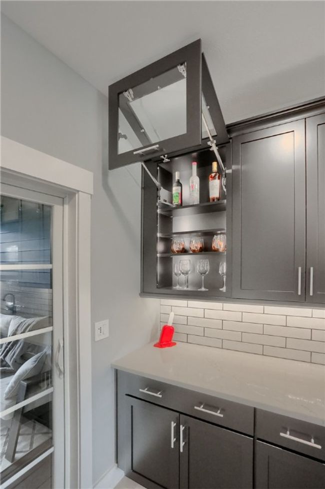 A built-in bar with lift-up glass cabinet doors offers the perfect modern touch, complete with open shelving for bottles and stemware, sleek tile backsplash, and under-cabinet lighting for a polished, entertaining-ready vibe. | Image 12