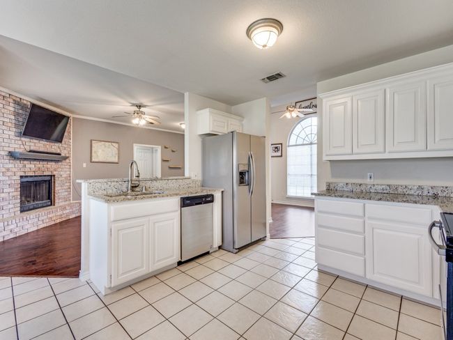 Kitchen featuring stainless steel appliances, ceiling fan, light tile patterned flooring, a sink, and a fireplace | Image 12