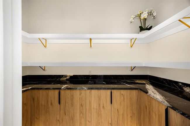 This spacious walk-in pantry offers both style and functionality with custom wood cabinetry, striking black stone countertops, and elegant veining that elevates the design. Open shelving with gold-accented brackets provides ample storage and display space, while under-shelf lighting potential enhances both visibility and ambiance. A perfect blend of luxury and practicality for any modern kitchen. | Image 13