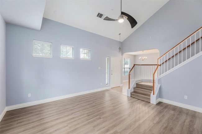 Unfurnished living room featuring stairs, light wood-style flooring, ceiling fan, high vaulted ceiling, and a chandelier | Image 8
