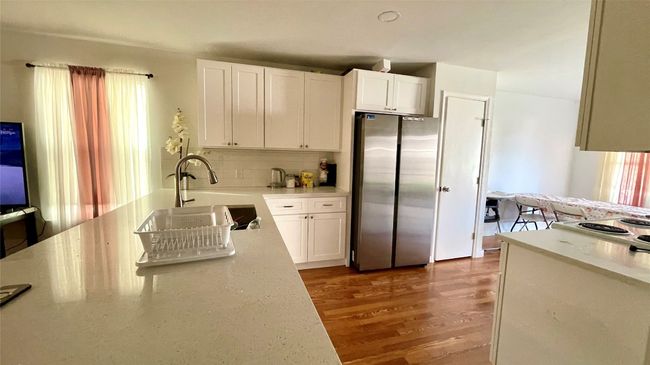 Kitchen with freestanding refrigerator, white cabinets, wood finished floors, and decorative backsplash | Image 18