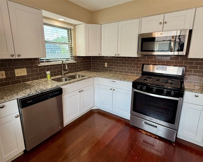 Kitchen with stainless steel appliances, a sink, dark wood finished floors, white cabinetry, and light stone counters | Image 8