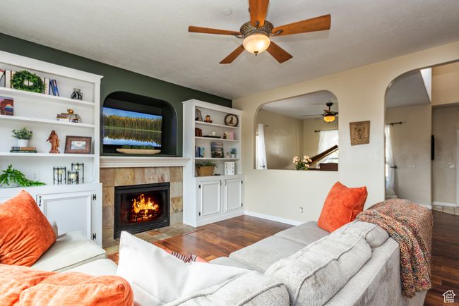 Living area featuring a ceiling fan, arched walkways, wood finished floors, and a tiled fireplace | Image 7