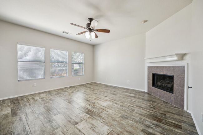 Unfurnished living room featuring ceiling fan, wood finished floors, and a gas log fireplace | Image 7