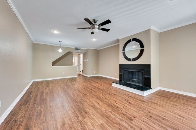 Unfurnished living room with a multi sided fireplace, baseboards, a ceiling fan, and wood finished floors | Image 11