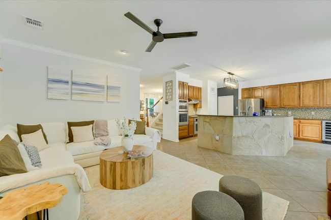Living area featuring a ceiling fan, light tile patterned floors, stairs, crown molding, and wine cooler | Image 8