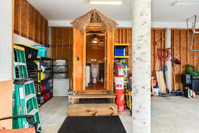 This photo showcases a garage ample storage space, and a unique tiki-style half bath. The area includes shelves, ladders, and tools, offering practical functionality. | Image 45