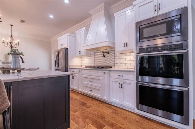 Kitchen with light stone countertops, white cabinetry, stainless steel appliances, and premium range hood | Image 10