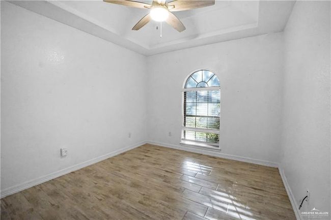 Empty room featuring a raised ceiling, wood finished floors, and ceiling fan | Image 4