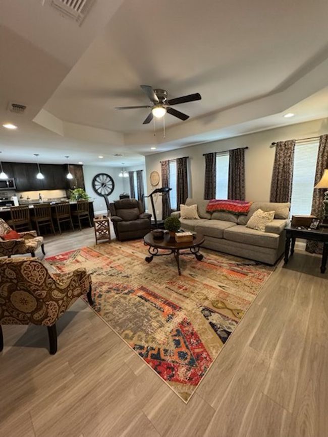 Living area with ceiling fan, a tray ceiling, light wood-style flooring, visible vents, and recessed lighting | Image 12