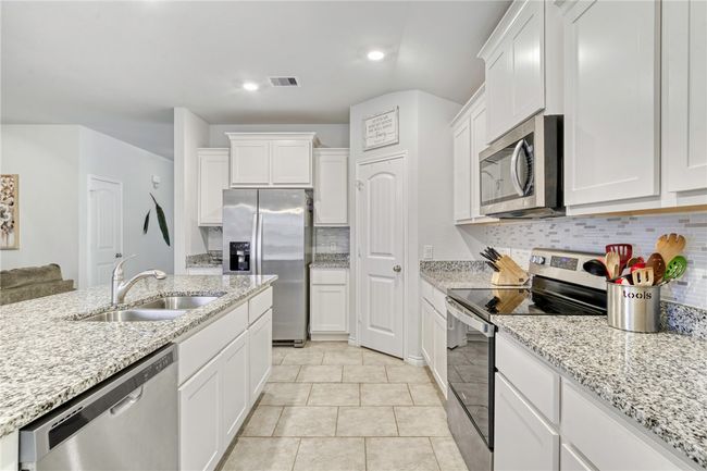 Kitchen featuring sink, light stone counters, tasteful backsplash, stainless steel appliances, and white cabinets | Image 14