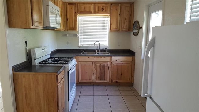 Kitchen featuring light tile patterned floors, a sink, white appliances, and dark countertops | Image 5