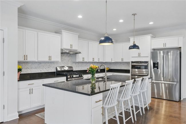 Gourmet kitchen seamlessly connected to the great room, featuring white cabinetry, granite countertops, stainless steel appliances, and a spacious island with pendant lighting. Open-concept layout provides a perfect flow for entertaining and everyday living. | Image 13