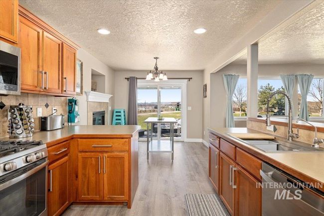 Kitchen with stainless steel appliances, a textured ceiling, a chandelier, a peninsula, and brown cabinets | Image 9