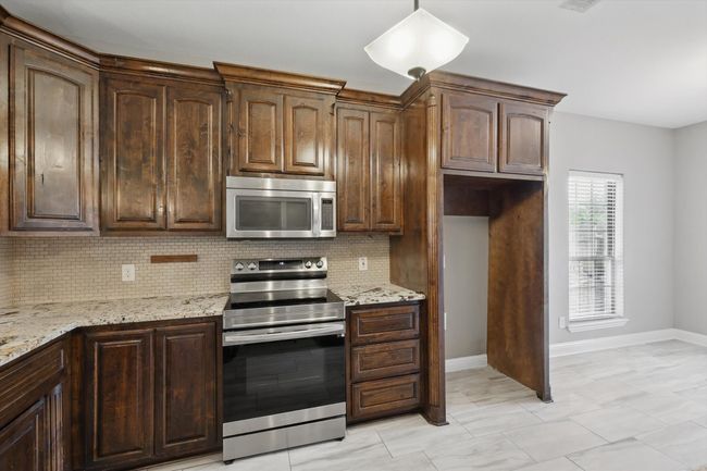 Kitchen featuring stainless steel appliances, decorative backsplash, baseboards, light stone countertops, and dark brown cabinetry | Image 6