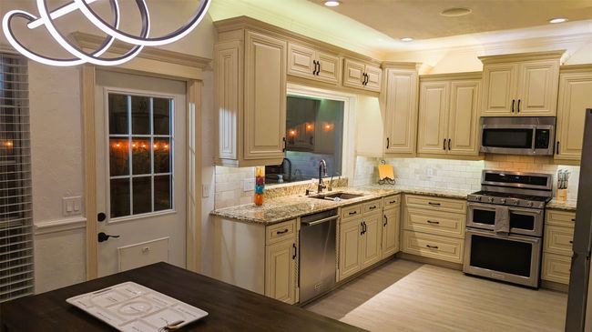 Kitchen featuring appliances with stainless steel finishes, cream cabinets, decorative backsplash, light stone countertops, and light wood-style floors | Image 7