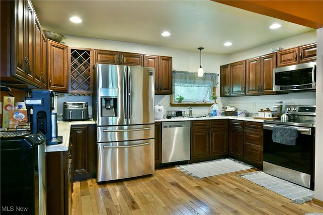 Kitchen featuring appliances with stainless steel finishes, light countertops, light wood-style flooring, hanging light fixtures, and a sink | Image 10