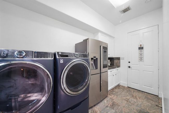 The utility room with space for a secondary refrigerator/freezer and access to the 3-car attached garage includes a painted cabinet with a stainless steel utility sink, upper and lower cabinet & drawer storage and tile flooring. | Image 40