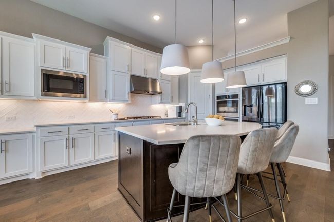 Kitchen featuring appliances with stainless steel finishes, under cabinet range hood, a sink, a kitchen island with sink, and light countertops | Image 13